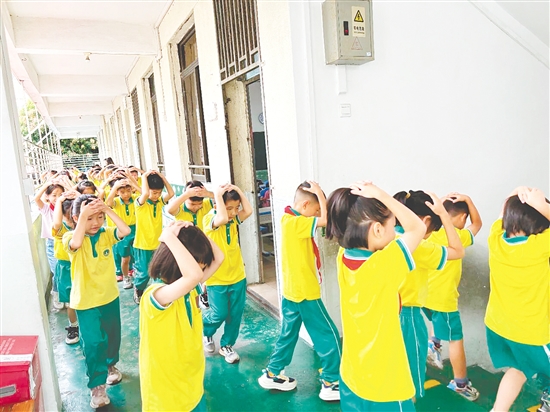 演練中，學生雙手抱頭、緊貼墻角，按照指定的逃生路線快速有序地撤離至操場安全區(qū)域。